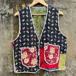 May include: A black quilted vest with a floral print and two pockets. The vest has a V-neck and is trimmed with a white and red striped fabric.