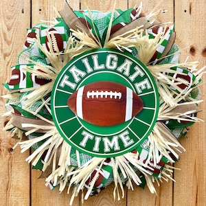 May include: A decorative wreath featuring green and white mesh, brown burlap ribbons, and straw-like accents. A central circular sign displays a brown football graphic with white laces and the text TAILGATE TIME in bold white capital letters.