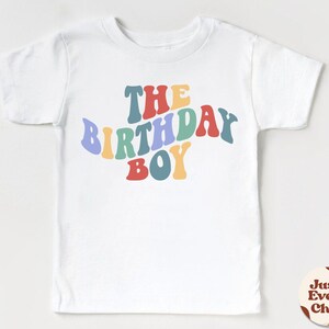 K&ouml;nnte beinhalten: Wei&szlig;es T-Shirt mit dem Text "The Birthday Boy" in Regenbogenfarben.