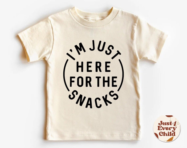 May include: A cream-colored short-sleeved t-shirt with black text that reads "I'm Just Here For The Snacks" in a circle.