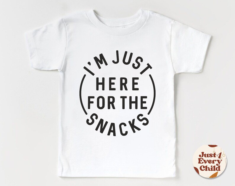 May include: White short-sleeved t-shirt with black text that reads "I'm Just Here For The Snacks" in a circle.