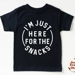 May include: Black short-sleeved t-shirt with white text that reads "I'm Just Here For The Snacks" in a circle.