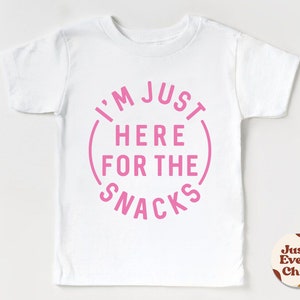 May include: White t-shirt with pink text that reads "I'm Just Here For The Snacks" in a circle.