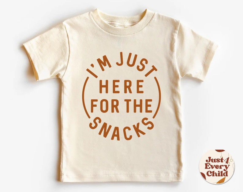 May include: A cream colored short-sleeved t-shirt with a brown circle graphic that says "I'm Just Here For The Snacks".