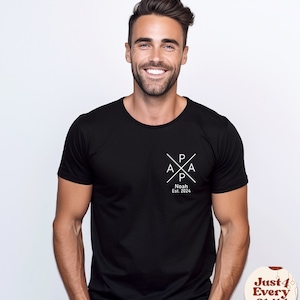 May include: A black short-sleeved t-shirt featuring a white graphic on the left chest. The graphic consists of the word PAPA arranged in a cross pattern with the text Noah Est. 2024 printed directly underneath the cross design in white lettering.