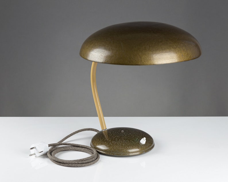 May include: A vintage green desk lamp with a mushroom-shaped shade and a wooden arm. The lamp has a white cord and plug.
