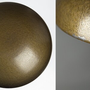 May include: A close-up of a gold-colored lampshade with a textured surface. The lampshade is round and has a slight curve to it.