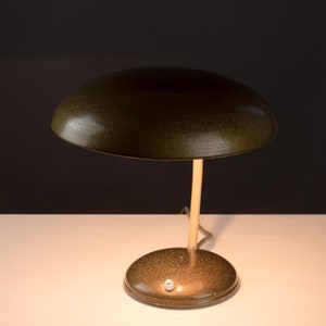 May include: A green metal desk lamp with a round, dome-shaped shade and a slender, beige stem. The lamp has a round base and a white switch.