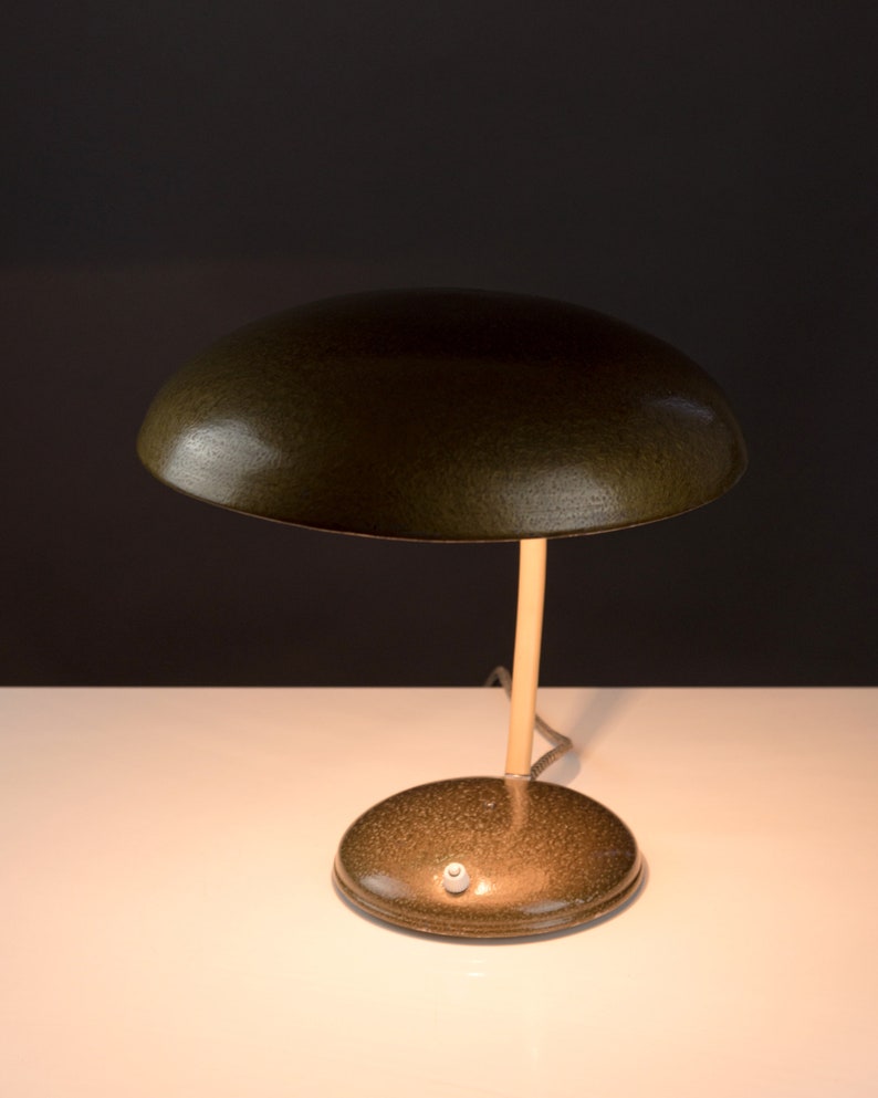 May include: A green metal desk lamp with a round, dome-shaped shade and a slender, beige stem. The lamp has a round base and a white switch.