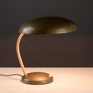 May include: A green metal desk lamp with a curved wooden arm and a round base. The lampshade is a rounded dome shape.