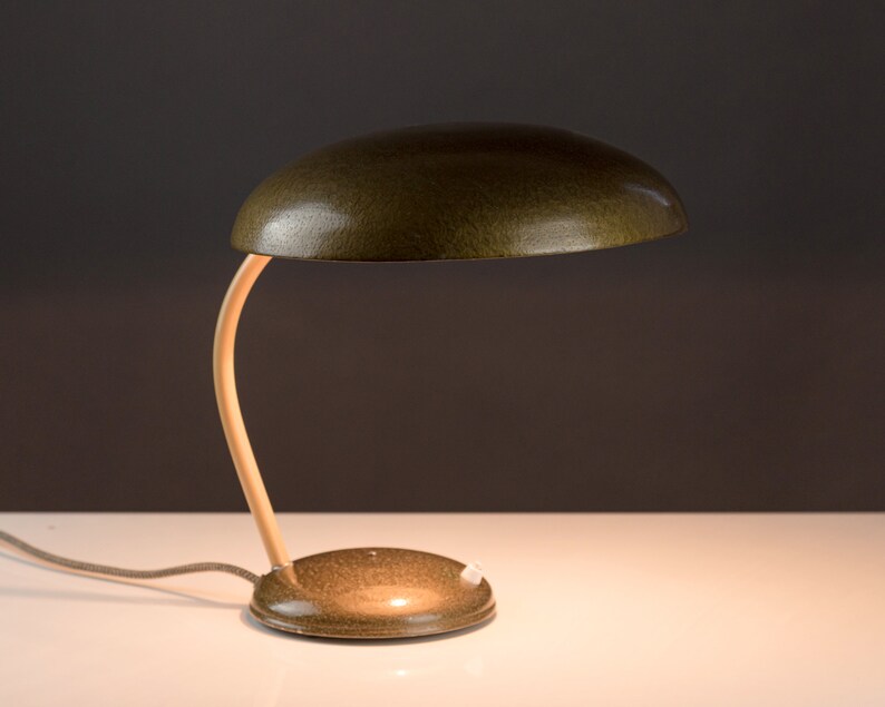 May include: A green metal desk lamp with a curved wooden arm and a round base. The lampshade is a rounded dome shape.