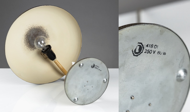 May include: A vintage desk lamp with a white metal shade and a wooden arm. The lamp has a silver base with a label that reads "418 01 250 V 60 W".