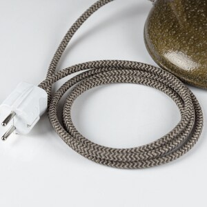 May include: A white electrical plug with two prongs and a ground pin, connected to a brown braided electrical cord.