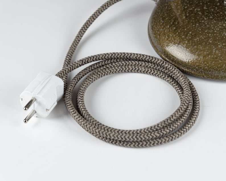 May include: A white electrical plug with two prongs and a ground pin, connected to a brown braided electrical cord.