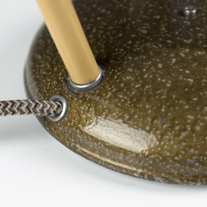 May include: Close-up of a green lamp base with a gold-colored metal arm and a black and white braided cord.