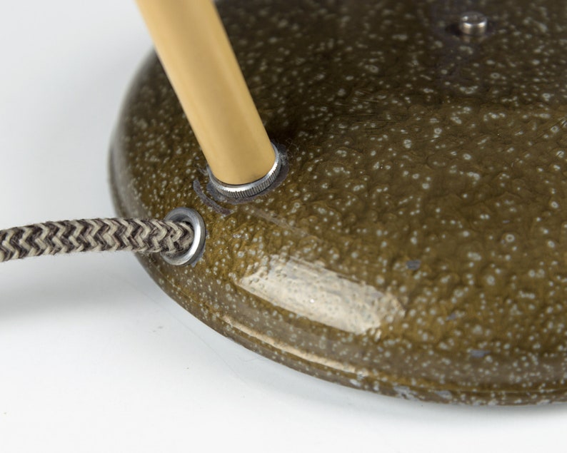 May include: Close-up of a green lamp base with a gold-colored metal arm and a black and white braided cord.