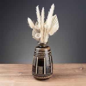Könnte beinhalten: Eine dekorative Keramikvase mit einem dunkelbraunen und cremefarbenen geometrischen Muster. Die Vase ist mit getrockneten cremefarbenen Blumen und Gräsern gefüllt. Die Vase steht auf einer Holzoberfläche.
