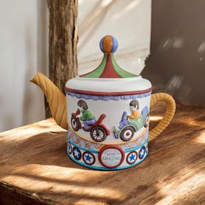 Può includere: Una teiera decorativa in ceramica a tema circo. La teiera presenta un corpo bianco con accenti colorati, tra cui un coperchio a righe rosse, verdi e arancioni e un manico e beccuccio gialli. Il design include illustrazioni di bambini su motociclette e la parola "AMAZING".