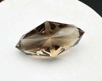 May include: A faceted, smoky quartz crystal with a light brown color. The crystal is cut into a unique, elongated shape with many facets.