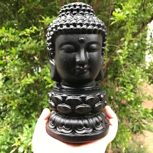 Puede incluir: Estatua de cabeza de Buda negra con una base de flor de loto. La estatua est&aacute; hecha de un material liso y oscuro y tiene una expresi&oacute;n serena.