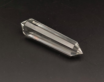 May include: A clear quartz crystal point, also known as a double terminated crystal, is a long, slender, and pointed crystal with facets on both ends. The crystal is lying on a black surface.