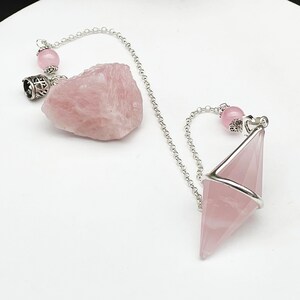 May include: A pink rose quartz crystal pendulum with a silver chain and a pink rose quartz crystal bead. The pendulum is shaped like a pyramid and is suspended from a silver chain. The chain is attached to a pink rose quartz crystal bead.