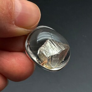 May include: A silver pendant with a clear resin dome containing a silver-colored mineral crystal.