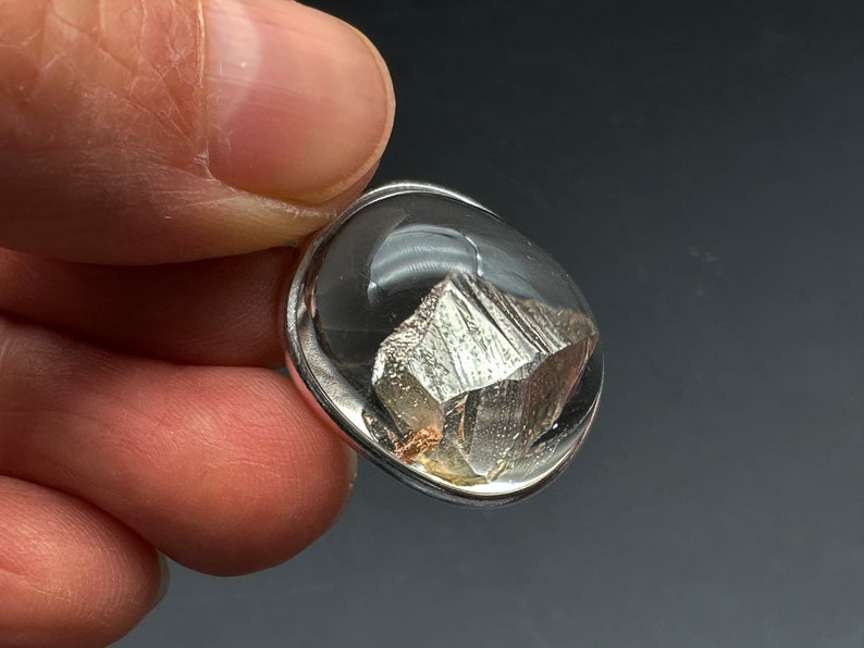 May include: A silver pendant with a clear resin dome containing a silver-colored mineral crystal.