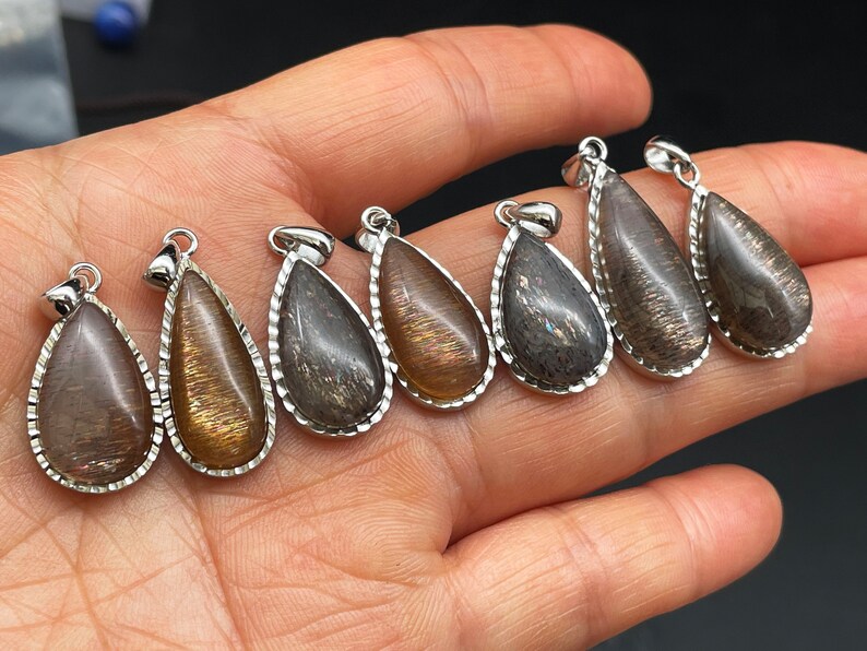 May include: Seven teardrop-shaped pendants with a silver-toned metal setting. The pendants are made of a dark brown stone with a shimmery, iridescent finish.