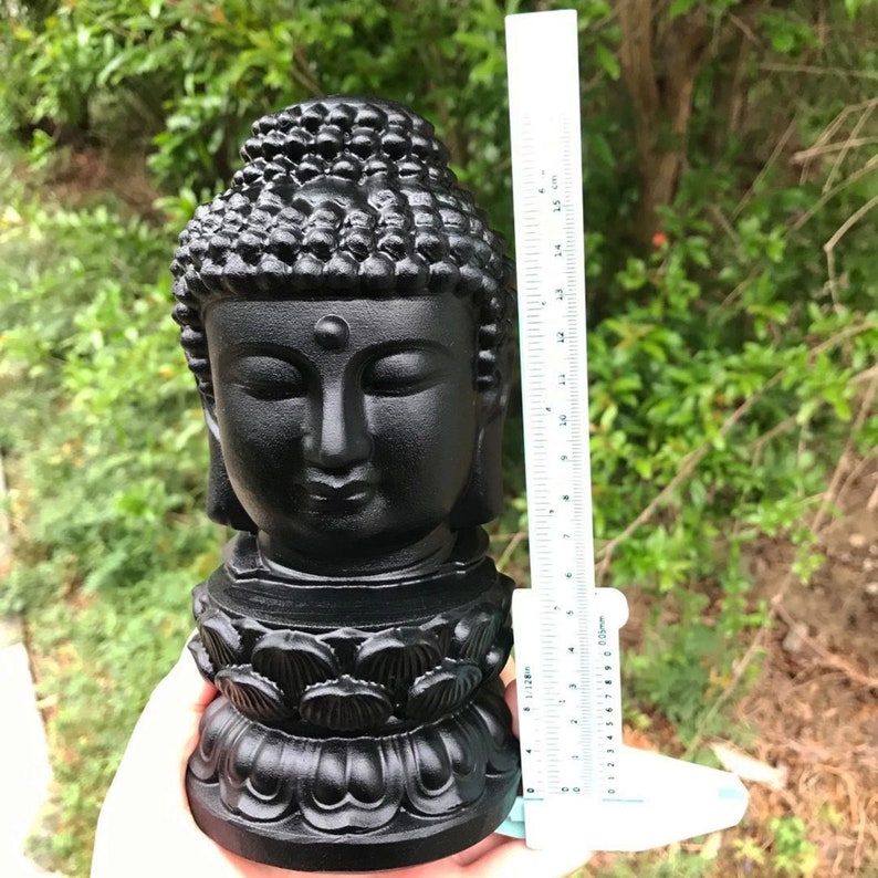 Puede incluir: Estatua de cabeza de Buda negra con una base de loto. La estatua mide aproximadamente 15 cm de alto.