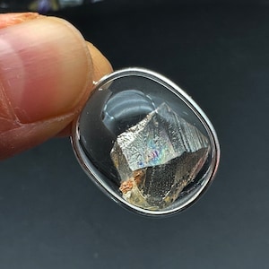 May include: A silver oval pendant with a clear glass setting containing a small, iridescent, metallic, crystal-like stone.