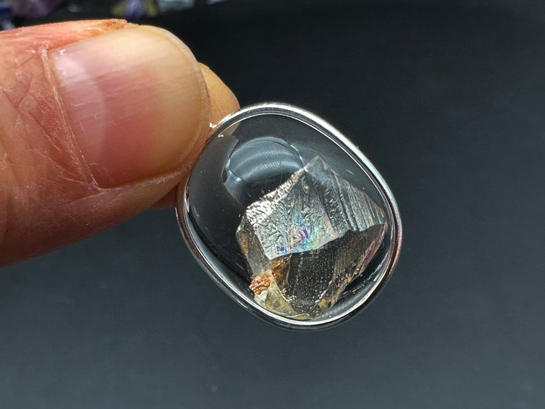 May include: A silver oval pendant with a clear glass setting containing a small, iridescent, metallic, crystal-like stone.