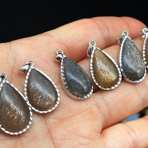 May include: Five teardrop-shaped pendants with silver settings and a dark brown, iridescent stone. The stones have a shimmery, glittery appearance.