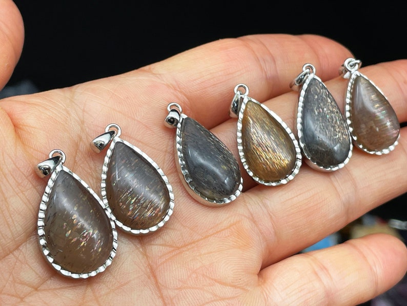 May include: Five teardrop-shaped pendants with silver settings and a dark brown, iridescent stone. The stones have a shimmery, glittery appearance.