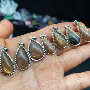 May include: Seven teardrop-shaped pendants with a silver setting and a gold and brown sunstone gemstone.