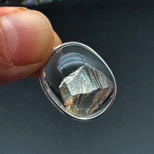 May include: A silver pendant with a clear glass oval setting containing a metallic gray, faceted crystal.