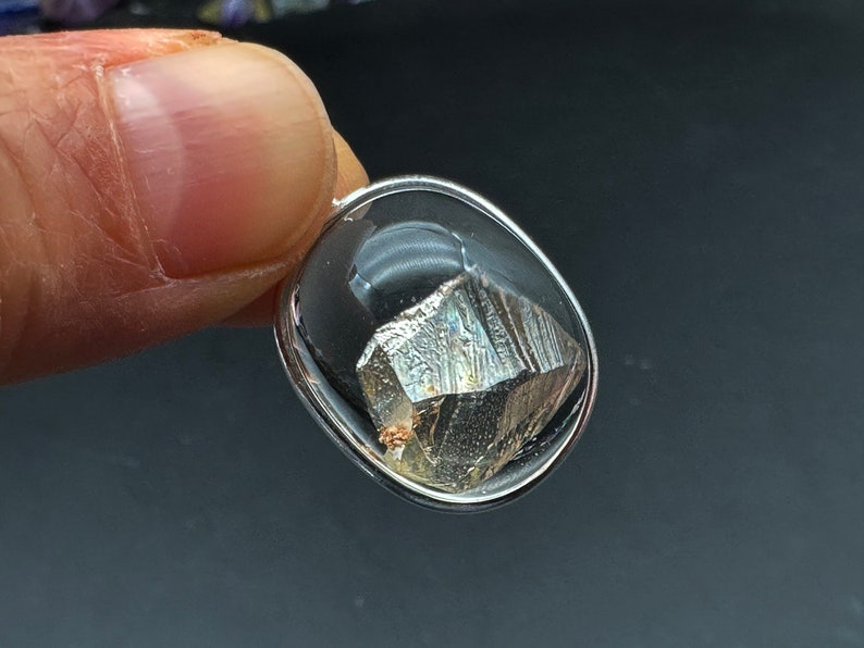 May include: A silver pendant with a clear glass oval setting containing a metallic gray, faceted crystal.