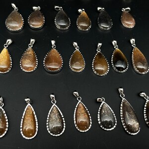 May include: A collection of 20 teardrop-shaped pendants with a silver-toned metal setting. The pendants are made of a brown and black iridescent gemstone.