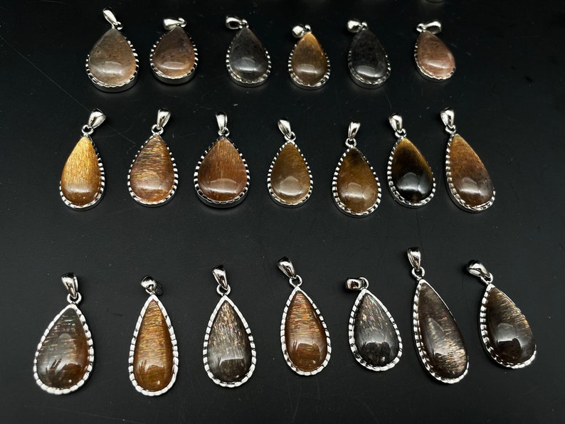 May include: A collection of 20 teardrop-shaped pendants with a silver-toned metal setting. The pendants are made of a brown and black iridescent gemstone.