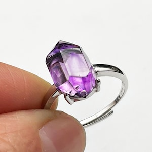 Könnte beinhalten: Ein silberner Ring mit einem violetten Amethyst-Edelstein in einer facettierten, spitzen Form.