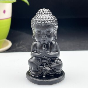May include: A small black statue of a meditating Buddha. The statue is sitting in a traditional meditation pose with hands clasped in front of the chest.