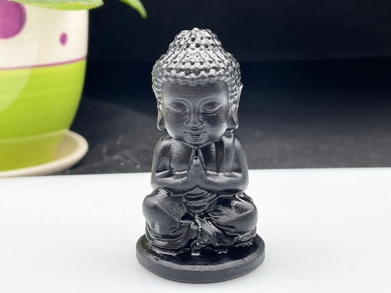 May include: A small black statue of a meditating Buddha. The statue is sitting in a traditional meditation pose with hands clasped in front of the chest.