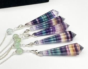 Op de afbeelding: Vijf zilveren kettingen met fluorite kristallen hangers. Elke hanger is een dubbel geëindigde punt met een regenboog van kleuren, waaronder paars, groen en geel. De kettingen zijn versierd met groene kralen.