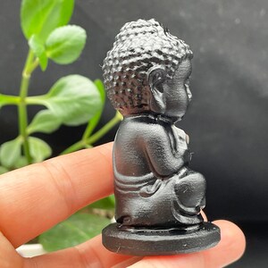 May include: A small black figurine of a meditating Buddha sitting cross-legged on a black base.