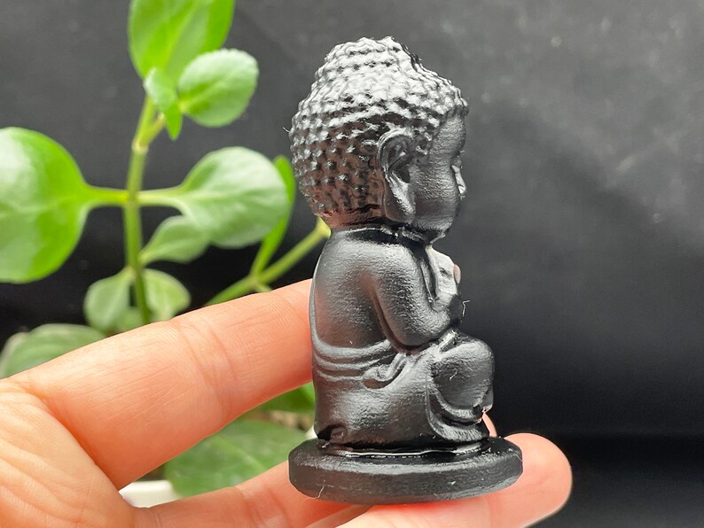 May include: A small black figurine of a meditating Buddha sitting cross-legged on a black base.