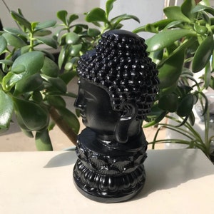 Puede incluir: Una escultura de busto negro y detallada de Buda con una cabeza redonda y una base de loto.