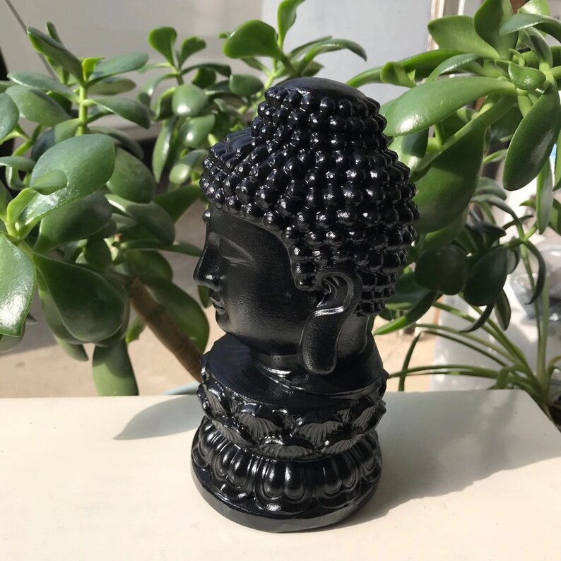Puede incluir: Una escultura de busto negro y detallada de Buda con una cabeza redonda y una base de loto.