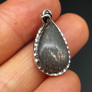 May include: A teardrop-shaped pendant with a silver setting and a dark gray iridescent stone.