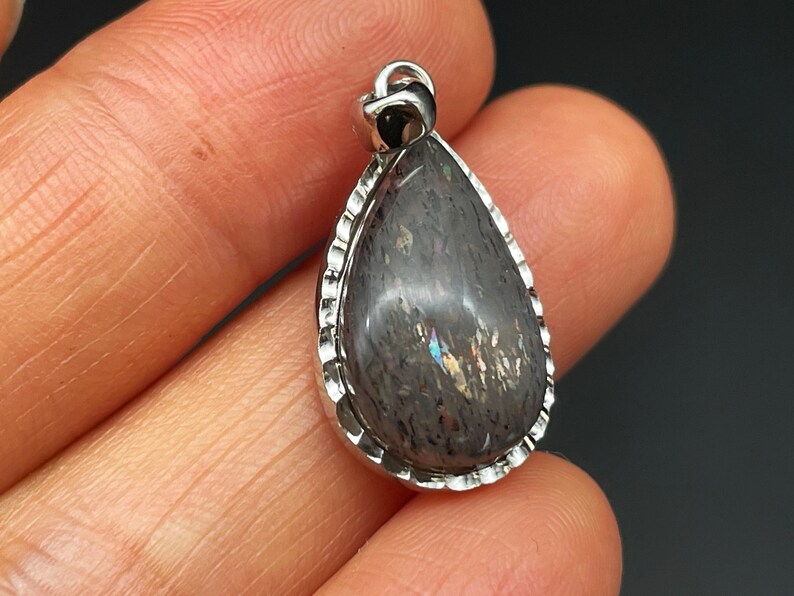 May include: A teardrop-shaped pendant with a silver setting and a dark gray iridescent stone.