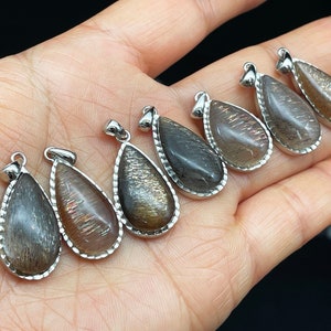 May include: Seven teardrop-shaped pendants with a silver-toned metal setting. The pendants are made of a dark, iridescent stone with a shimmery, metallic finish.